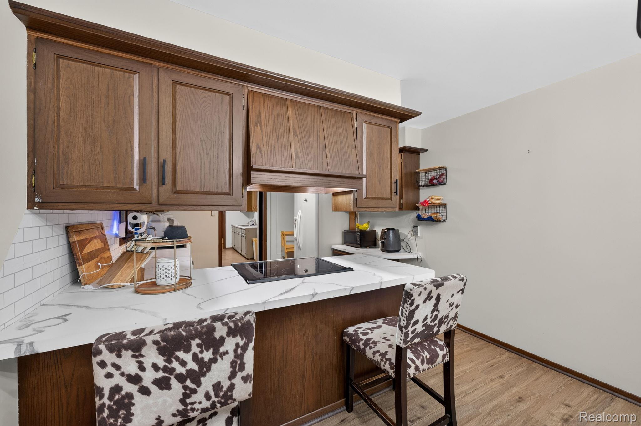 5330 Sheridan Road Saginaw, MI 48601 - Photo 17 of 50 Kitchen breakfast bar featuring a smooth cooktop, white marble-look countertop, wood-finish cabinetry, and white subway tile backsplash