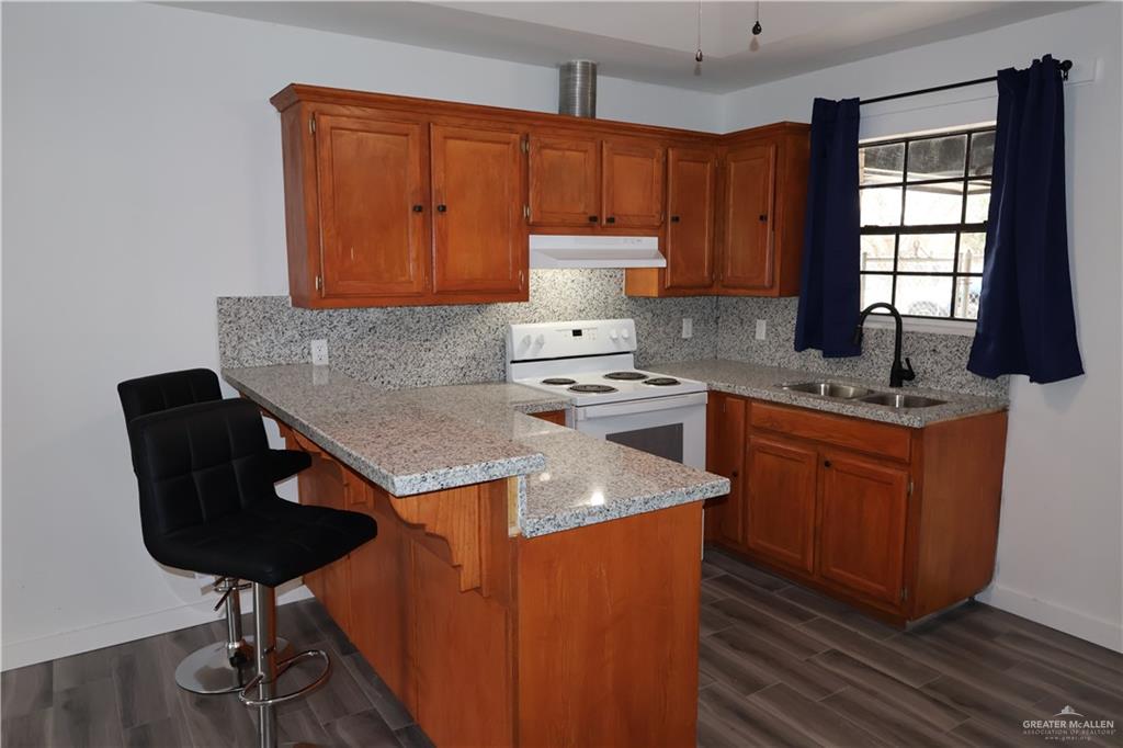 3526 Paseo Del Rey Edinburg, TX 78542 - Photo 5 of 20 Kitchen with white range with electric stovetop, a kitchen breakfast bar, wood finish cabinetry, a peninsula, and dark wood-type flooring