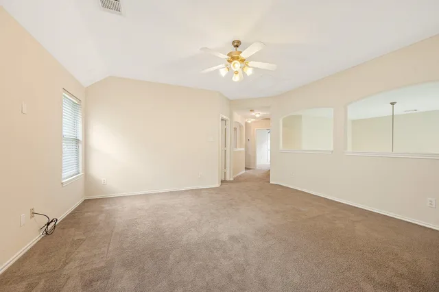 an empty room with chandelier fan and windows