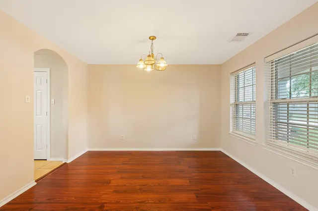 a big room with wooden floor a chandelier fan and windows