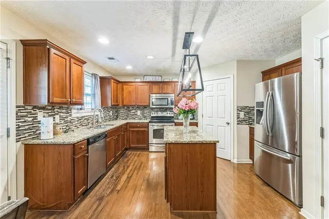 a kitchen with granite countertop a refrigerator a sink dishwasher a stove and a oven with wooden floor