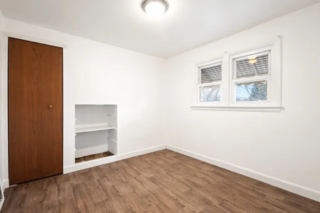 an empty room with wooden floor closet and windows