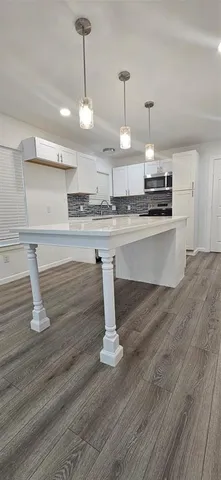 a large kitchen with kitchen island a stove a sink dishwasher a dining table and chairs with wooden floor