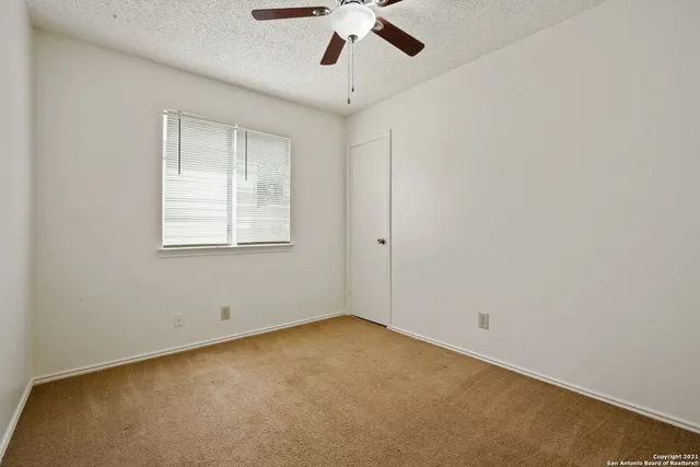 an empty room with a chandelier fan and windows