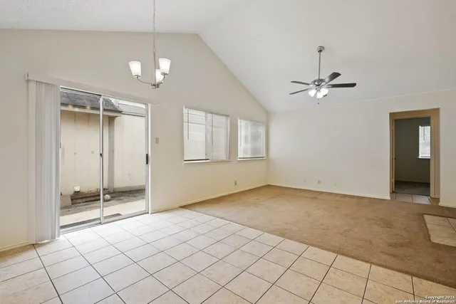 an empty room with chandelier fan and windows