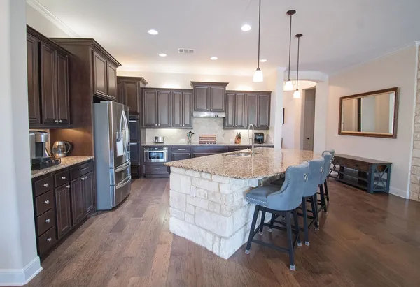 a kitchen with stainless steel appliances granite countertop wooden cabinets a refrigerator a sink a stove a dining table and chairs