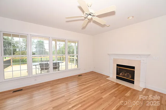 a view of an empty room with wooden floor fireplace and a window