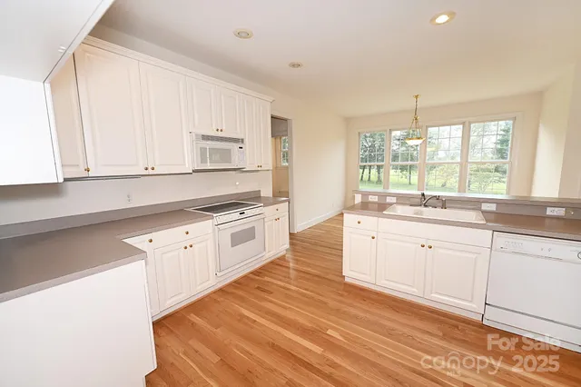 a kitchen with granite countertop white cabinets white appliances a sink and a large window