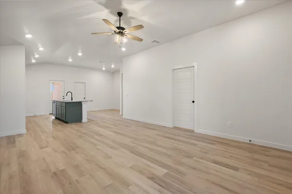 a view of an empty room with wooden floor and a ceiling fan