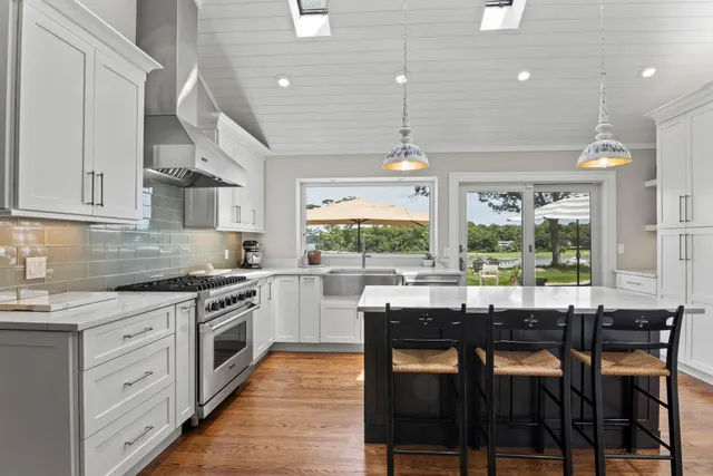 a kitchen with stainless steel appliances granite countertop a stove top oven a sink with white cabinets and wooden floor