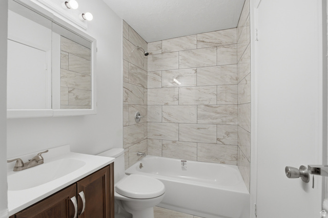 7910 Woolley Way Magna, UT 84044 - Photo 10 of 26 Bathroom featuring a white bathtub with tile surround, a built-in vanity with a dark wood-finish cabinet, a white countertop, and a mirrored medicine cabinet