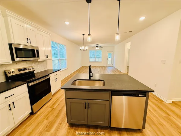 a kitchen with stainless steel appliances granite countertop a sink a microwave a stove and a wooden floors