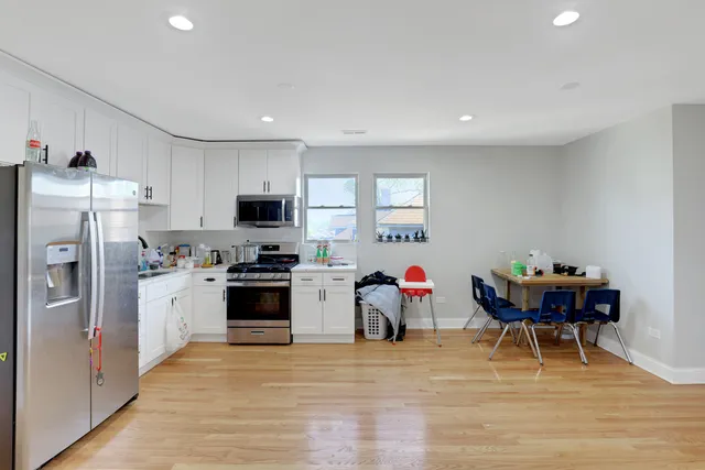 a kitchen with stainless steel appliances a stove a sink dishwasher a refrigerator and a dining table with wooden floor