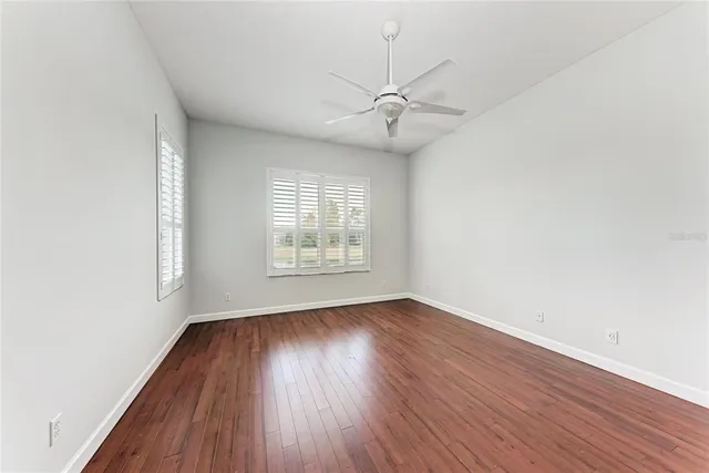 an empty room with wooden floor fan and windows