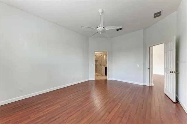an empty room with wooden floor ceiling fan and window