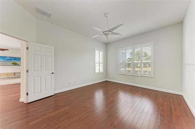 an empty room with wooden floor chandelier fan and windows