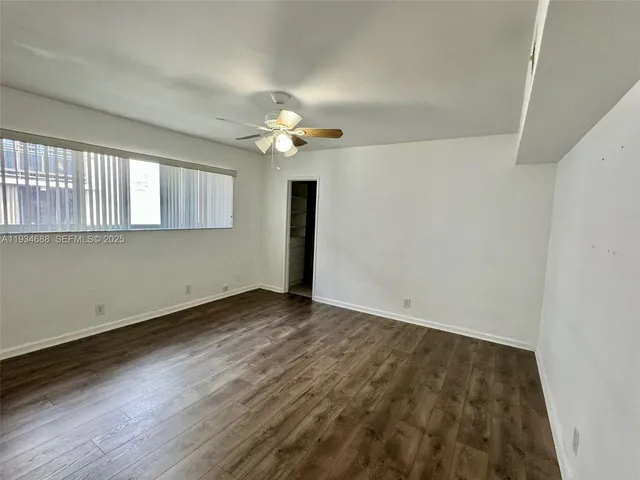 an empty room with wooden floor chandelier fan and windows