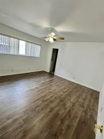 an empty room with wooden floor chandelier fan and windows