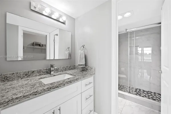 a bathroom with a granite countertop sink a mirror and shower