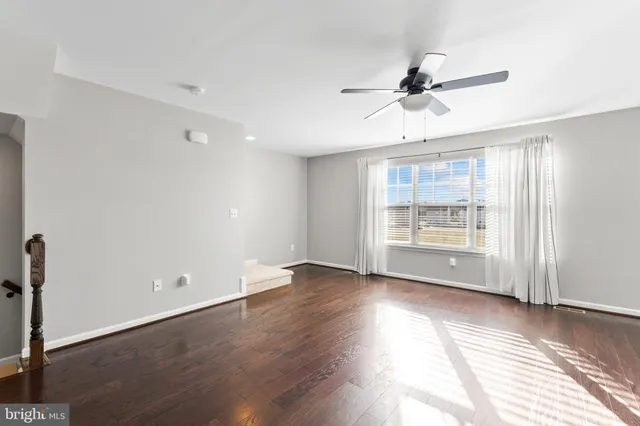an empty room with wooden floor fan and windows