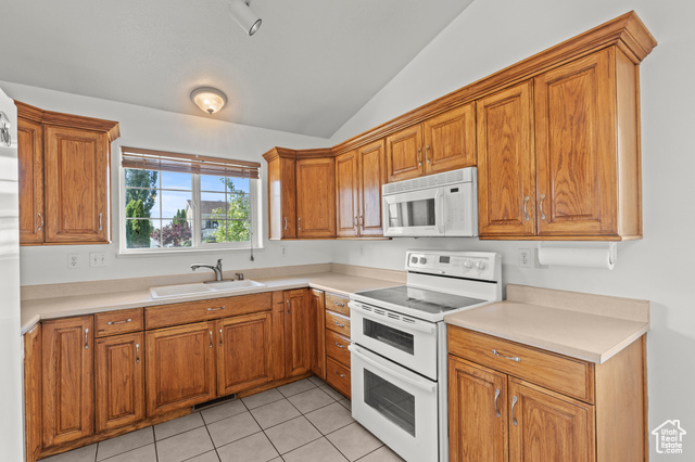1099 Three Point Avenue Logan, UT 84321 - Photo 8 of 27 Kitchen featuring white appliances, lofted ceiling, brown cabinetry, light tile patterned flooring, and light countertops