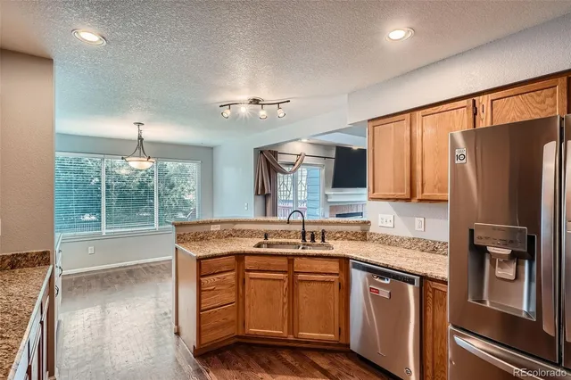 a kitchen with stainless steel appliances granite countertop a refrigerator a sink dishwasher a stove and white countertops with wooden floor