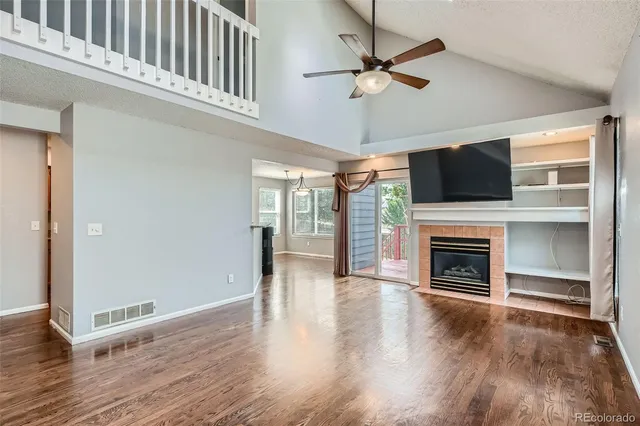 an empty room with wooden floor a fireplace a ceiling fan and windows