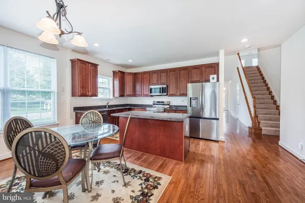 a kitchen with stainless steel appliances granite countertop a stove top oven a sink a dining table and chairs with wooden floor