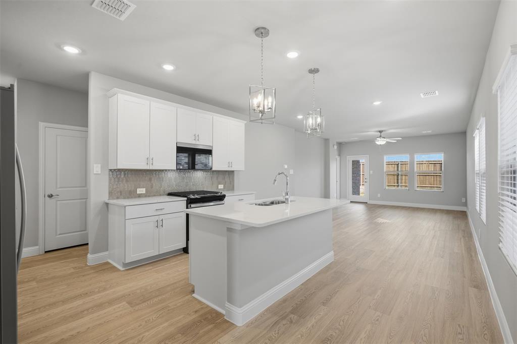 1701 Arches Road Anna, TX 75409 - Photo 4 of 19 Contemporary kitchen featuring white cabinetry, a central island with a sink, stainless steel appliances, and wood-finish flooring