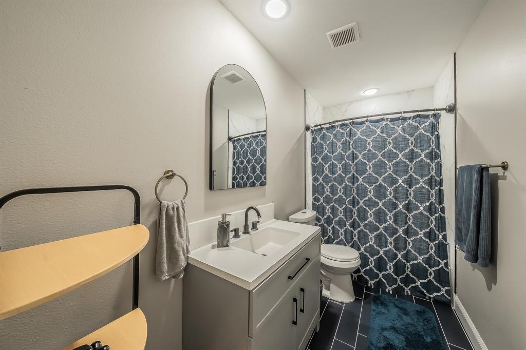 117 Rock Salt Drive Springtown, TX 76082 - Photo 27 of 38 Bathroom featuring a white integrated sink vanity with dark hardware, a framed arched mirror, and white tiled walls surrounding the shower area