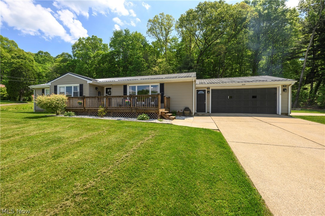 Single-story residence featuring light-toned siding, a deep front deck with railing, and a two-car garage with dark paneled doors