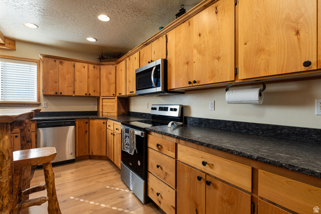 Kitchen featuring stainless steel appliances, a textured ceiling, recessed lighting, dark countertops, and light wood finished floors