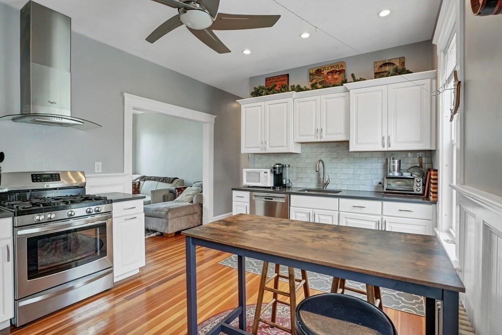 a kitchen with stainless steel appliances granite countertop a stove top oven a sink dishwasher and white cabinets with wooden floor