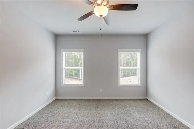 an empty room with chandelier fan and windows