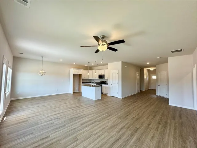 a view of an empty room and kitchen view with wooden floor