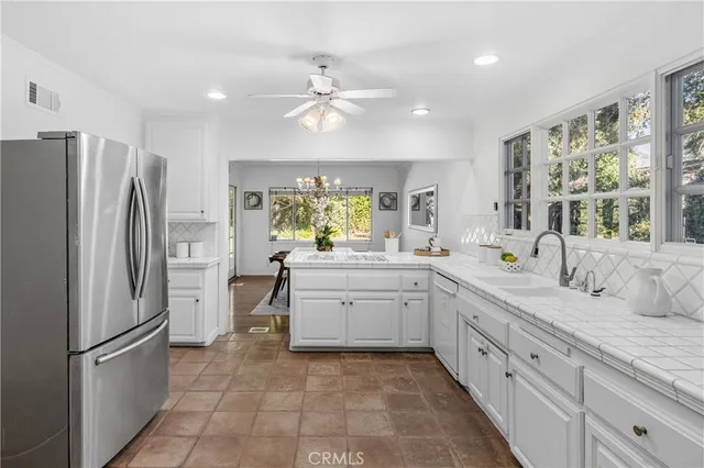a large white kitchen with a refrigerator a sink dishwasher a stove and white cabinets with wooden floor