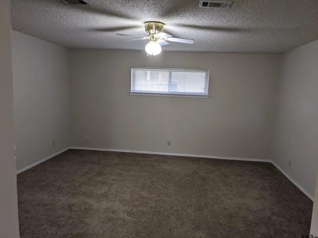 an empty room with a chandelier fan and windows