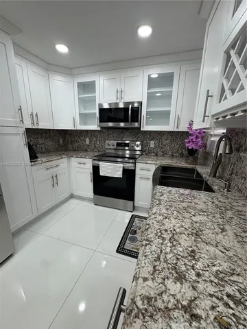 a kitchen with granite countertop a stove top oven a sink a counter space and cabinets