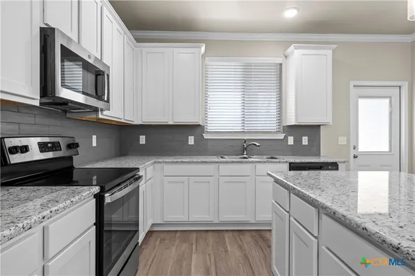 a kitchen with stainless steel appliances granite countertop a stove a sink a microwave a refrigerator and white cabinets with wooden floor
