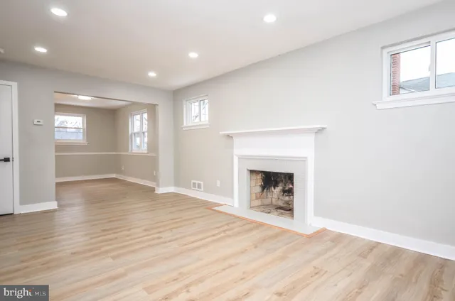 a view of an empty room with wooden floor fireplace and a window