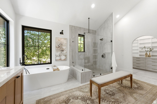 3027 Homestead Road Park City, UT 84098 - Photo 26 of 62 Modern bathroom featuring a freestanding soaking tub with black fixtures, a spacious walk-in shower with a glass enclosure and built-in bench, a large window with black framing, and neutral-toned wall and floor tiling