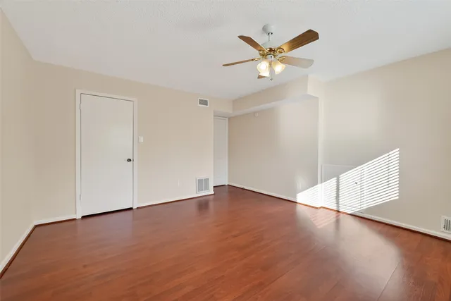 an empty room with wooden floor fan and windows
