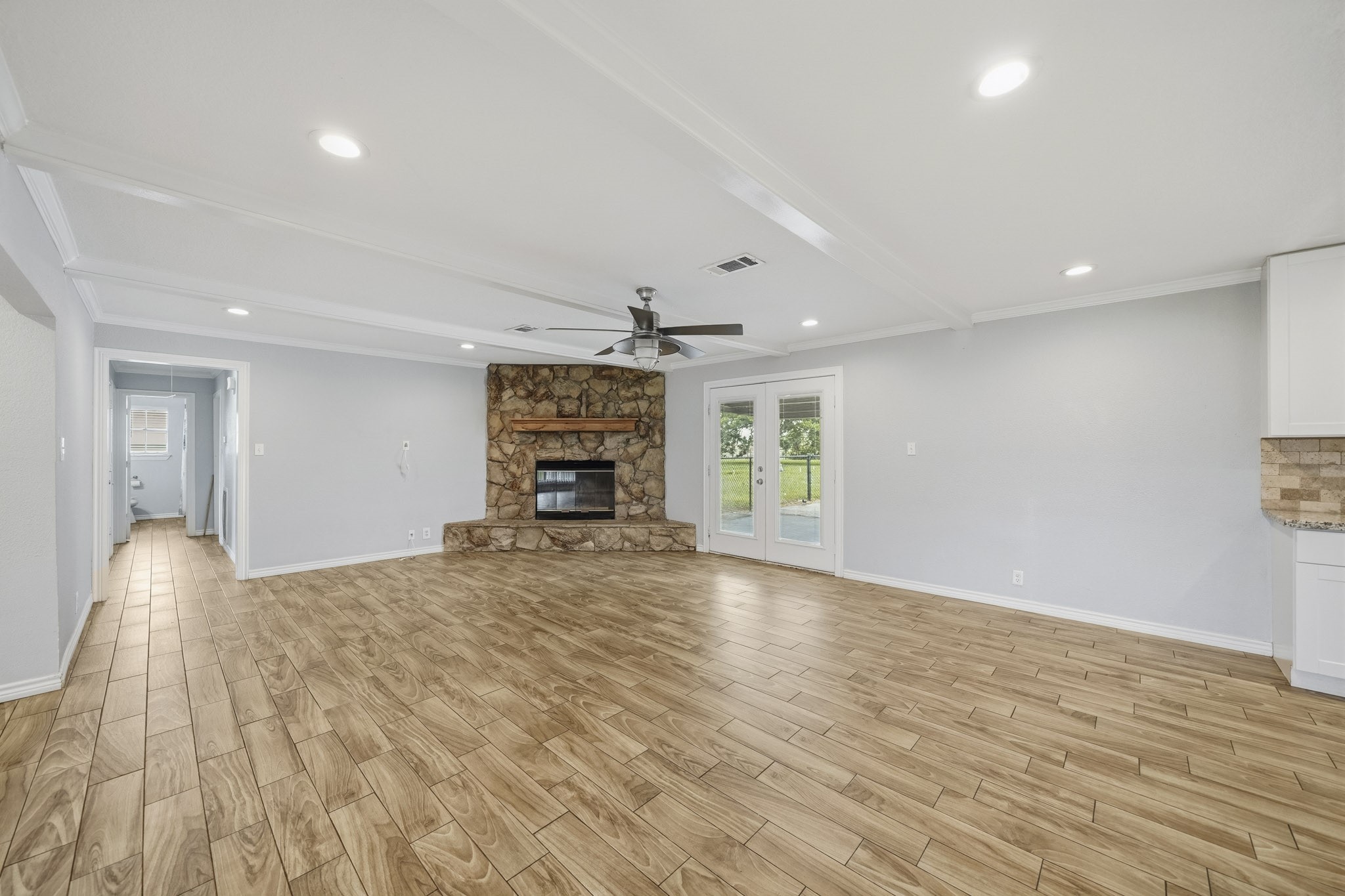 302 Country Road 893 Angleton, TX 77515 - Photo 11 of 26 This spacious living area features wood-look tile flooring, a stone fireplace, and a ceiling fan. French doors lead to an outdoor space, providing ample natural light. The neutral color palette and open layout offer a versatile setting for any decor style.