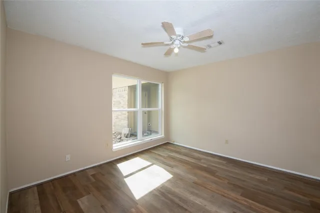 an empty room with wooden floor fan and windows