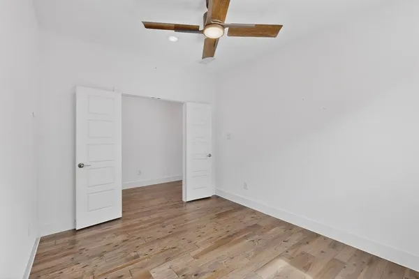 an empty room with wooden floor ceiling fan and window