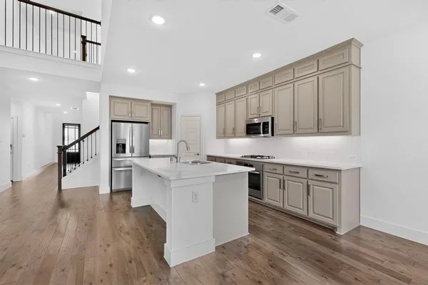 a kitchen with stainless steel appliances granite countertop a stove top oven a sink dishwasher and a refrigerator with wooden floor