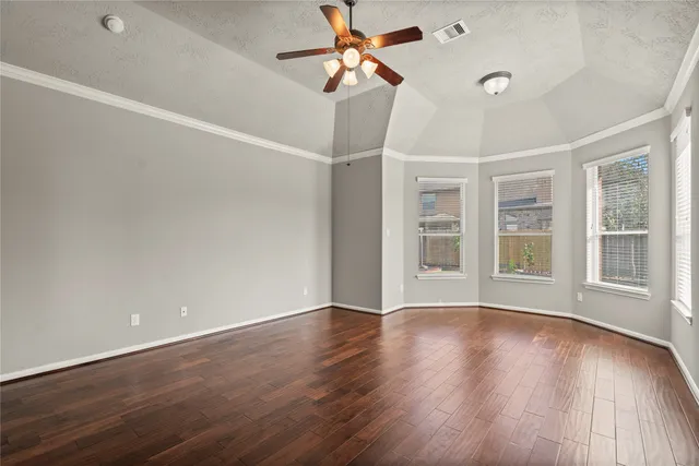 a view of an empty room with wooden floor and a ceiling fan