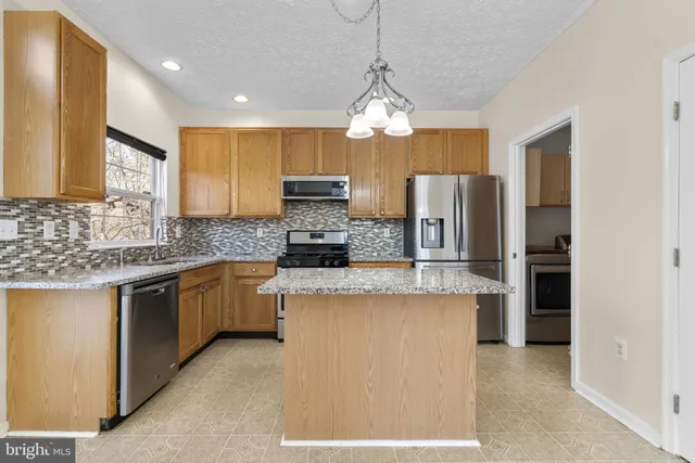 a kitchen with kitchen island granite countertop stainless steel appliances a stove a refrigerator a sink dishwasher a oven with white cabinets and couches