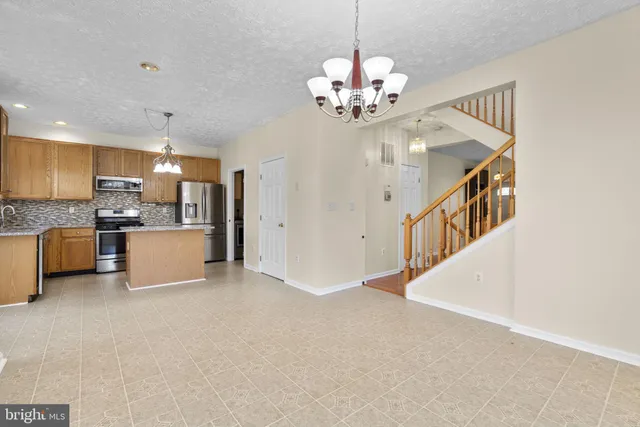 a open kitchen with stainless steel appliances granite countertop a refrigerator a stove and a chandelier