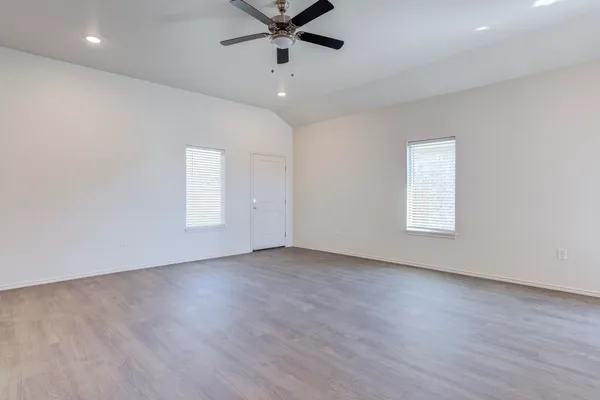 an empty room with wooden floor fan and windows